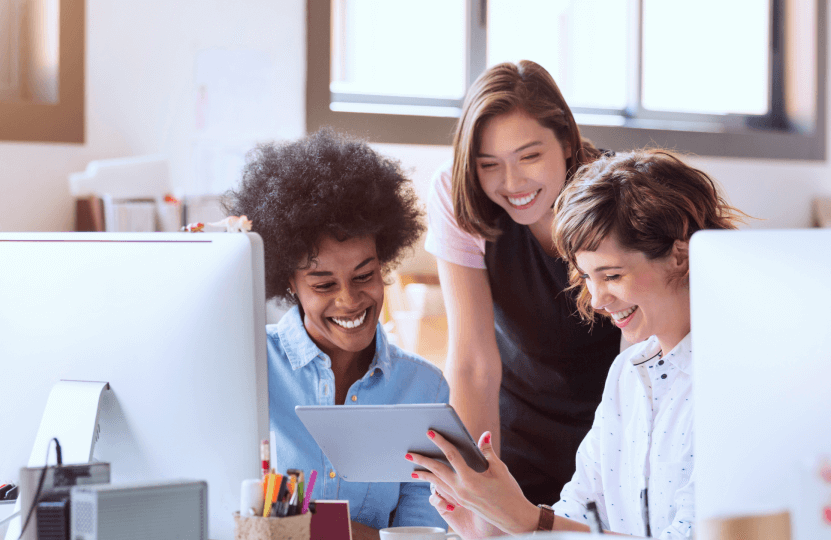 three women looking at a tablet and smiling