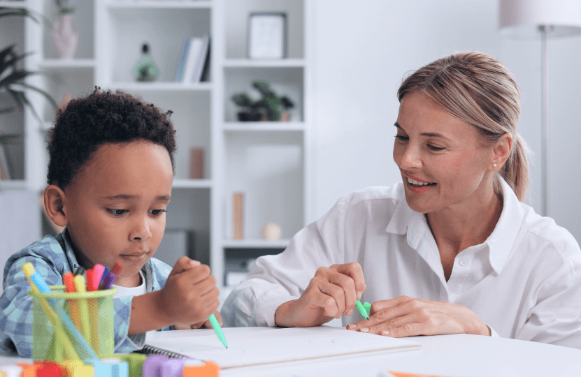 a kid writing on his notebook while a woman teaches him