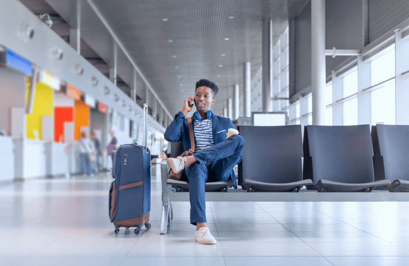 a man talking on the phone while he is on the airport with a travelbag