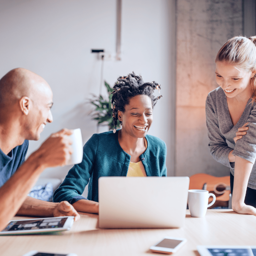 three people smiling while looking at the laptop screen